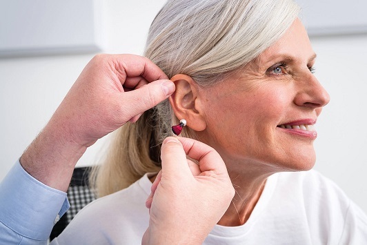 Ältere Frau erhält Hörgerät, Hörakustiker passt modernes Hörgerät im Ohr an.